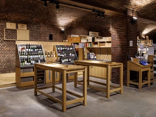 Cologne wine cellar Kellerraum mit Weinen, Holzregalen und Verkostungstischen aus hellem Holz, umgeben von Backsteinwänden.Cellar room with wines, wooden shelves and tasting tables made of light-colored wood, surrounded by brick walls.