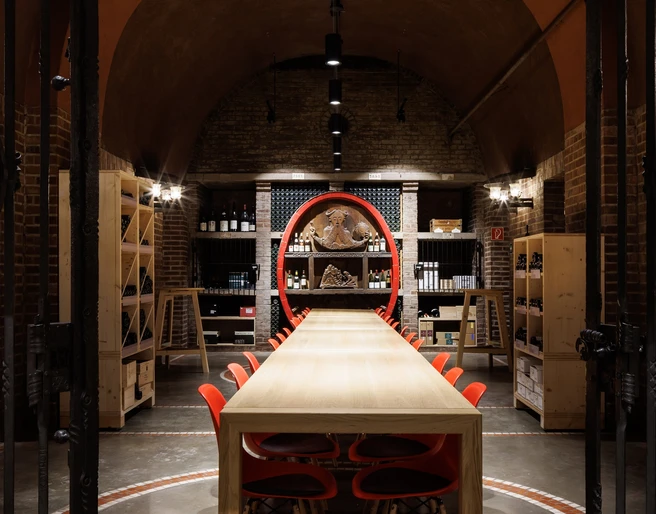 Cologne wine cellar Langer Holztisch mit roten Stühlen in einem stimmungsvoll beleuchteten Weinkeller.Long wooden table with red chairs in an atmospherically lit wine cellar.