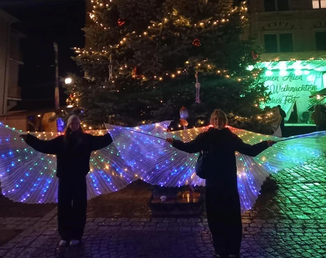 Weihnachtsmarkt Bad Lausick - Weihnachten in der Region Leipzig  Ein Weihnachtsbaum in Bad Lausick, beleuchtet und flankiert von Menschen mit leuchtenden Flügeln.