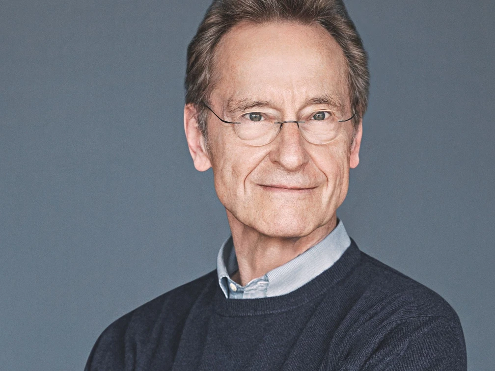 Literatur zur Nacht_Bernhard Schlink (c) Gaby Gerster Diogenes Verlag.jpg Schriftsteller Bernhard Schlink vor grauem Hintergrund, lächelnd, trägt Hemd und Pullover.