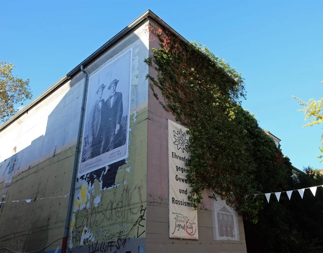 BunkerK101 Graffiti-verzierter Bunker mit großen Wandbildern und satt begrünten Ecken unter blauem Himmel.Graffiti-decorated bunker with large murals and lush green corners under a blue sky.