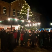 Weihnachten mit dem OBV Apen Menschenmenge bei Nacht auf einem festlich beleuchteten Weihnachtsmarkt vor einem großen Baum.