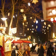Weihnachtsmarktstände in der festlich beleuchteten Innenstadt mit einigen Besuchern.