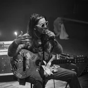 Bonanzafest Eine Person sitzt auf einem Stuhl und spielt Gitarre, während sie singt. Sie trägt eine Sonnenbrille und ist umgeben von Kerzenlicht.A person sits on a chair and plays the guitar while singing. She is wearing sunglasses and is surrounded by candlelight.