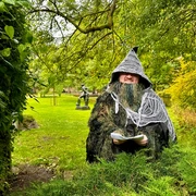 Naturetales premiere: "Alva in the land of shadows" Eine verkleidete Person in einem magischen Waldumfeld, umgeben von grünem Laub und Bäumen.A disguised person in a magical forest setting, surrounded by green foliage and trees.