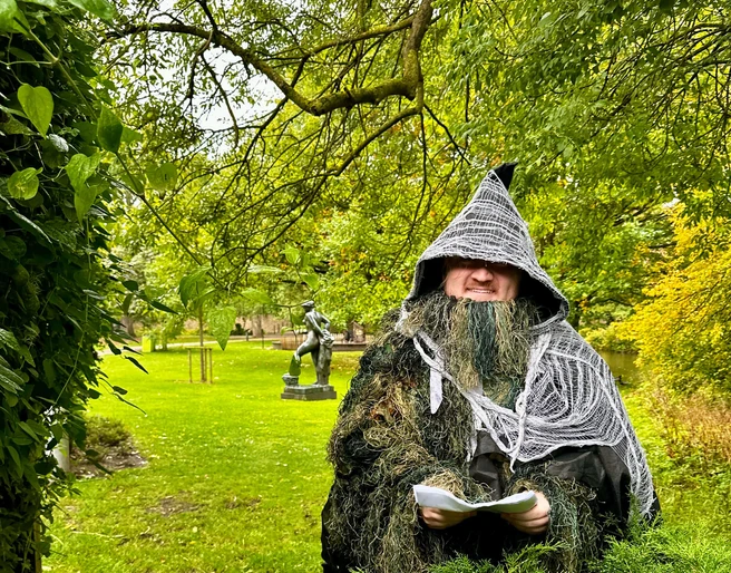 Naturetales premiere: "Alva in the land of shadows" Eine verkleidete Person in einem magischen Waldumfeld, umgeben von grünem Laub und Bäumen.A disguised person in a magical forest setting, surrounded by green foliage and trees.