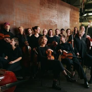 Ensemble Resonanzraum Ein Ensemble von Musiker*innen in schwarzer Kleidung posiert in einem modernen Raum, lächelnd.An ensemble of musicians dressed in black poses in a modern room, smiling.