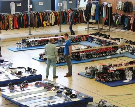 In einer Turnhalle sind Verkaufsflächen mit Schneesportbekleidung und -ausrüstung ausgestellt.