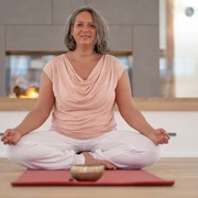 4 - DSC07588.jpg Frau sitzt entspannt im Schneidersitz auf einer Yogamatte vor einem Kamin und meditiert.