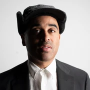 Patrice Eine Person mit dunklem Anzug und weißem Hemd, lächelt leicht. Schwarze Kappe auf dem Kopf.A person in a dark suit and white shirt, smiling slightly. Black cap on his head.