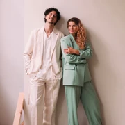 Daria Assmus & Marco Silvestri Zwei Musiker vor einer schlichten Wand, beide in eleganten Anzügen, lächeln entspannt.Two musicians in front of a plain wall, both in elegant suits, smiling relaxedly.