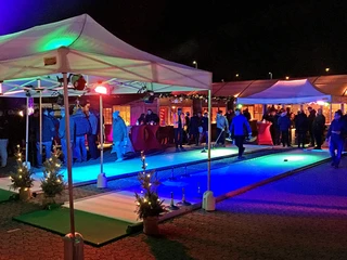 mSa Mobiler Weihnachtsmarkt Eisstockschießen-Bahn unter Pagodenzelten bei Nacht – Teamspaß und Networking auf dem mobilen Weihnachtsmarkt von mSa events für Unternehmen.Curling rink under pagoda tents at night - team fun and networking at mSa events' mobile Christmas market for companies.