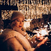 Weihnachtssingen-Bad-Zwischenahn.jpg Frau mit Wollmütze hält Wunderkerze unter festlicher Lichterdekoration beim Weihnachtssingen.