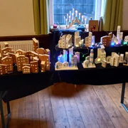 Tisch mit selbstgebastelten Geschenkideen Holzmodelle von Häusern und beleuchtete Stadtsilhouetten auf zwei Tischen in einem hellen Raum.