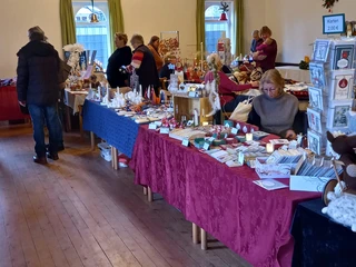Adventsbasar im Schützenhof (3).jpg Verkaufsstände mit handgefertigten Weihnachtsartikeln und Besuchern in einer festlich geschmückten Halle