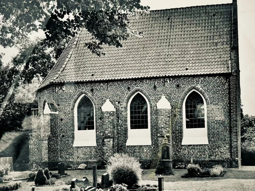 Erlebnistour Kapelle Vreschen-Bokel.jpg Historische Backsteinkapelle mit Spitzbogenfenstern, umgeben von Bäumen und gepflegtem Friedhof in schwarz-weiß