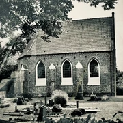 Erlebnistour Kapelle Vreschen-Bokel.jpg Historische Backsteinkapelle mit Spitzbogenfenstern, umgeben von Bäumen und gepflegtem Friedhof in schwarz-weiß