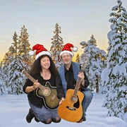 Dreebladd.png Zwei Personen knien im Schnee vor verschneiten Tannen, tragen Weihnachtsmützen und halten jeweils eine Gitarre.