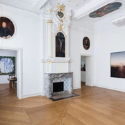 Kunsthaus NRW © Carl Brunn.jpg Museum mit einem Kamin in einem lichtdurchfluteten Raum. Die hohen, weiß gestrichenen Wände sind mit kunstvollen Gemälden dekoriert, darunter ein Porträt und abstrakte Kunstwerke. Holzboden verleiht dem Raum Wärme und Eleganz.