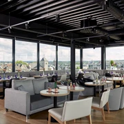 Innside Aachen Up Town Bar Lounge Raum mit Sofas, runden Tischen und Stühlen und Fensterfront mit Blick über Aachener Dächer.