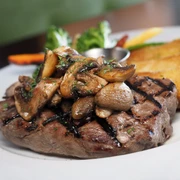 Steak, auf dem gebratene Champignons liegen, und Salat im Hintergrund.