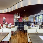 NOVO² - Novotel Aachen City Innenraum mit Sitzgruppen und einer Theke mit hohen Barstühlen.