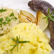 Teller mit Kartoffelpüree, Sauerkraut, einer Zwiebel und Wurst.