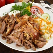 Teller mit Geschnetzeltem, Krautsalat, Gurke, Tomate, Zwiebeln, Peperoni, Salat und einem Dip.