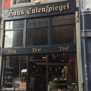 Dunkle Fassade mit der Aufschrift "Haus Eulenspiegel" und "Tea", "Tee" und "Thé" darunter. Hinter dem Schaufenster im Erdgeschoss ist Ware ausgestellt. Der Eingang befindet sich in der Mitte.
