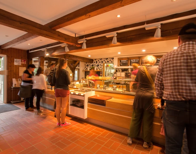 milchhalle-innen Besucher stehen am Tresen eines gemütlichen Cafés mit Backsteinwänden und hölzernen Deckenbalken.