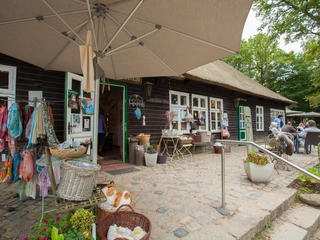milchhalle-wilsede-souvenirs Korb voller Schals und Filzartikel unter großen Sonnenschirmen vor einem historischen Haus.
