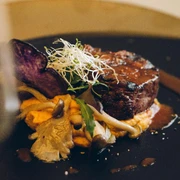 Steak in einer Soße auf einem Teller garniert mit Pilzen und Sprossen.