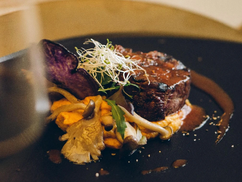 Restaurant Luna Steak in einer Soße auf einem Teller garniert mit Pilzen und Sprossen.