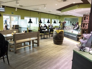 Einladendes Restaurant mit Holzbänken und gelb-grüner Dekoration, Gäste sitzen an Tischen.