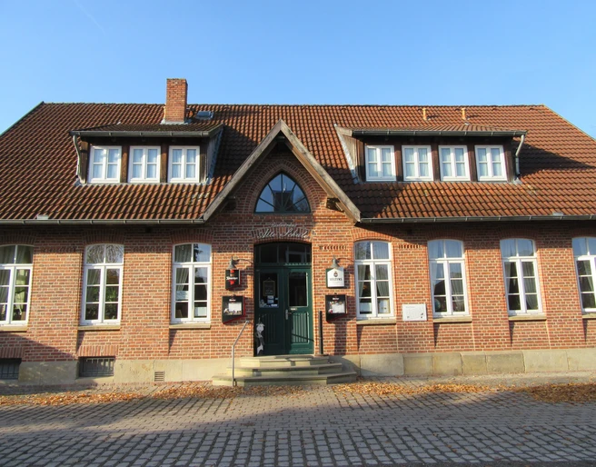 Ein Backsteingebäude mit hohen Fenstern und Schildern über dem Eingang unter einem Giebeldach.