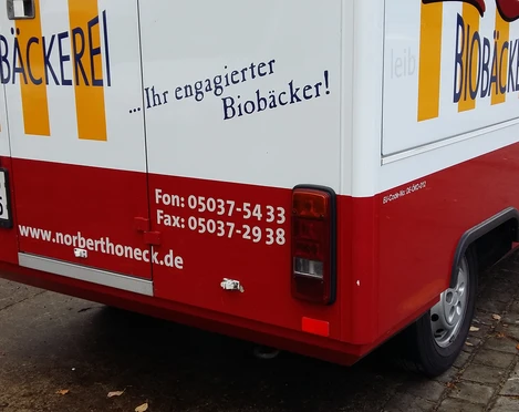 Café Honeck Seitliche Rückansicht eines roten Verkaufsanhängers der Biobäckerei Honeck auf gepflastertem Boden.