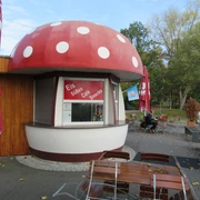 Fliegenpilz Mardorf Ein kleines Café in Mardorf mit fliegenpilzförmigem Dach, umgeben von einladenden Sitzgelegenheiten.