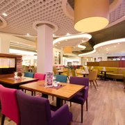 Innenbereich Cafe Möbel Eilers Ein geschmackvoll eingerichtetes Café mit hellen Holztischen, farbenfrohen Polsterstühlen und warmem Licht zaubert eine einladende Atmosphäre.