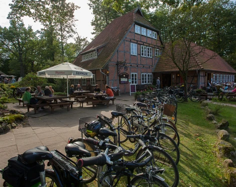 gasthaus-zum-heidemuseum-mit-terrassen Historisches Fachwerkhaus mit sonniger Terrasse und Fahrrädern im Vordergrund vor bewaldeter Kulisse.