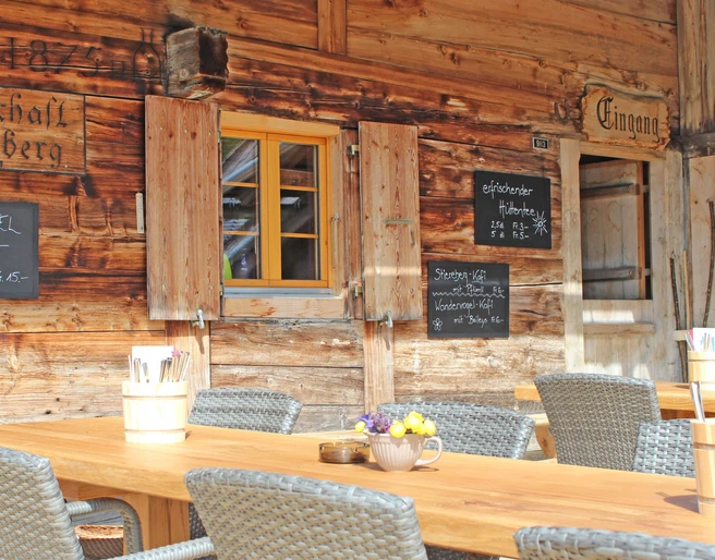 Stierenberg mountain restaurant terrace with summer sun Holztisch mit grauen Stühlen vor der Hauswand des GasthofsWooden table with gray chairs in front of the house wall of the innTable en bois avec chaises grises devant le mur de l'auberge