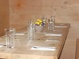 Gedeckter Tisch mit Bergblumendekoration  Gedeckter Holztisch mit Bergblumen in einer HolzstubeWooden table set with mountain flowers in a wooden parlourTable en bois dressée avec des fleurs des montagnes dans une salle à manger en bois