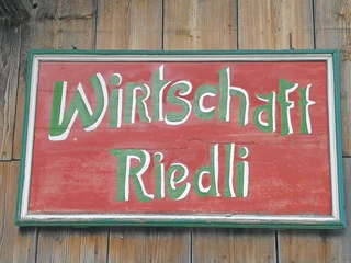 Shield of the restaurant Riedli  Rotes Holzschild mit der grün-weissen Aufschrift Riedli WirtschaftRed wooden sign with the green and white inscription Riedli WirtschaftPanneau en bois rouge avec l'inscription vert-blanc Riedli Wirtschaft
