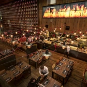 The Ash Blick von der Empore Blick von oben auf Innenraum mit vielen Tischgruppen und Stühlen, einer Theke, einem schmalen, längliche Bildschirm mit Flammen und einem großen Wandregal voller Weinflaschen.