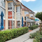 carpe-diem_ambulante-pflege-juli-2018-14 Mehrstöckiges Gebäudekomplex mit Balkonen, großen Fenstern und Café, umgeben von einem Gehweg und Grünflächen.