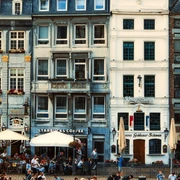 Vier schmale, mindestens dreistöckige Häuser stehen aneinandergereiht auf dem Marktplatz in Aachen. In den Erdgeschossen befinden sich Gastronomien, wovon eine das Restaurant Goldener Schwan ist. Vor den Lokalen stehen Sitzgruppen und Schirme.