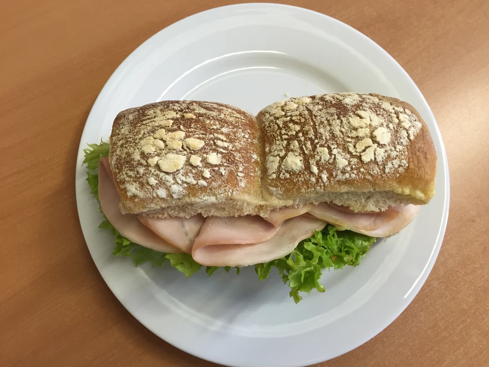belegtes Brötchen Frisches Brötchen mit Salatblatt und saftigem Schinken auf einem weißen Teller angerichtet.