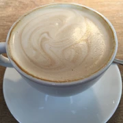 Kaffeetasse Kaffeetasse mit schaumiger Milchoberfläche auf Holztisch, begleitet von einem Teelöffel.