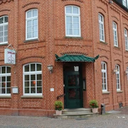 Shanghai Rotes Backsteingebäude mit grünem Eingang und mehreren Fenstern, gelegene an einem gepflasterten Gehweg.