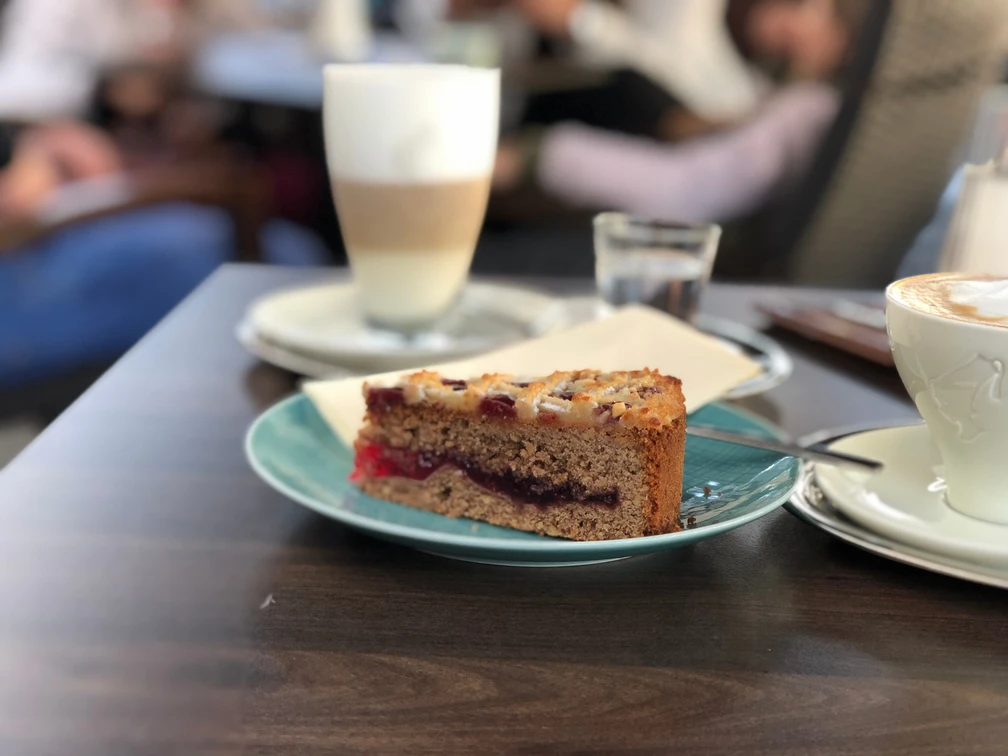 Kuchenstück Ein Stück Streuselkuchen mit roter Füllung auf einem blauen Teller, im Hintergrund ein Café.