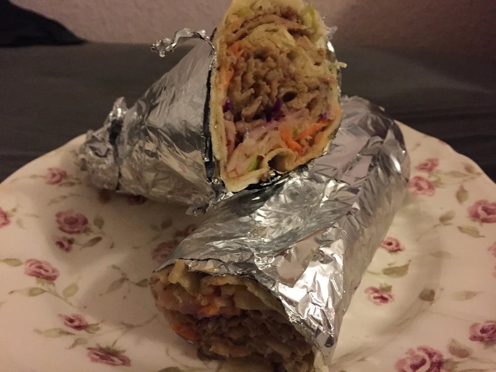 Ein auf einem Teller platzierter Döner Rollo, gefüllt mit saftigem Fleisch und frischem Gemüse.